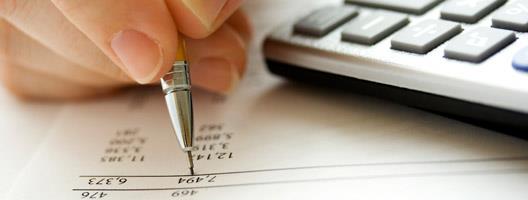 Person writing on a paper with finance numbers in front of computer keyboard