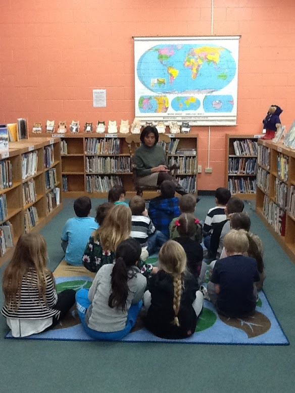 The librarian sitting on a rocking chair reading a book to students sitting on a rug in front of her. The librarian sitting on a rocking chair reading a book to students sitting on a rug in front of her.